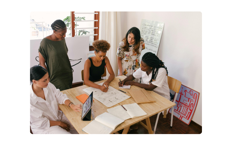 Diverse group of women entrepreneurs discussing target market insights for eCommerce growth around a wooden table.